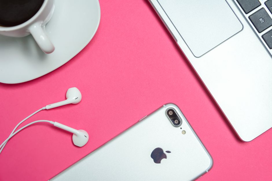 A modern workspace with laptop, smartphone, and coffee cup on a vibrant pink background.